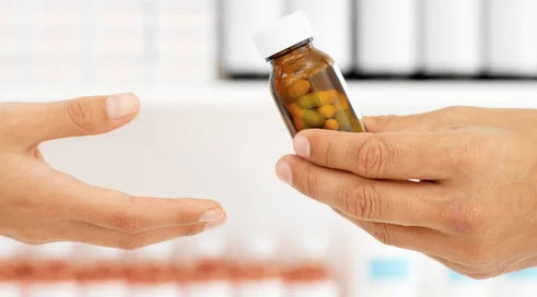 Close up of the hands of a pharmacist giving a patient a bottle of pills