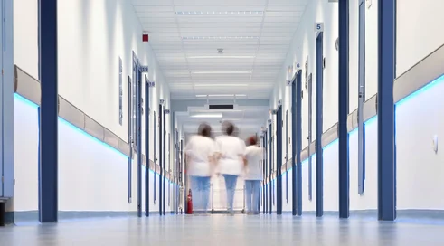 three blurred figures in medical uniforms walking away in hospital corridor