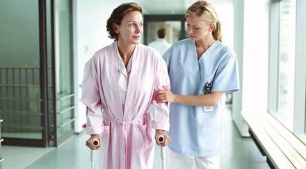 Female nurse holding patient using crutches in hospital corridor