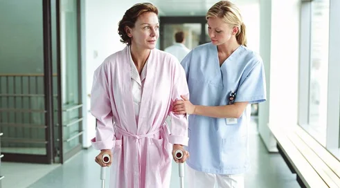 Female nurse holding patient using crutches in hospital corridor
